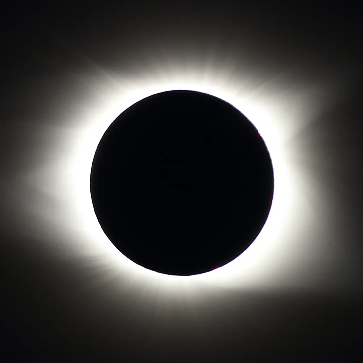 Fotografia de eclipse solar total: disco escuro da Lua cobre o Sol, cercado pela coroa luminosa contra o céu escuro.