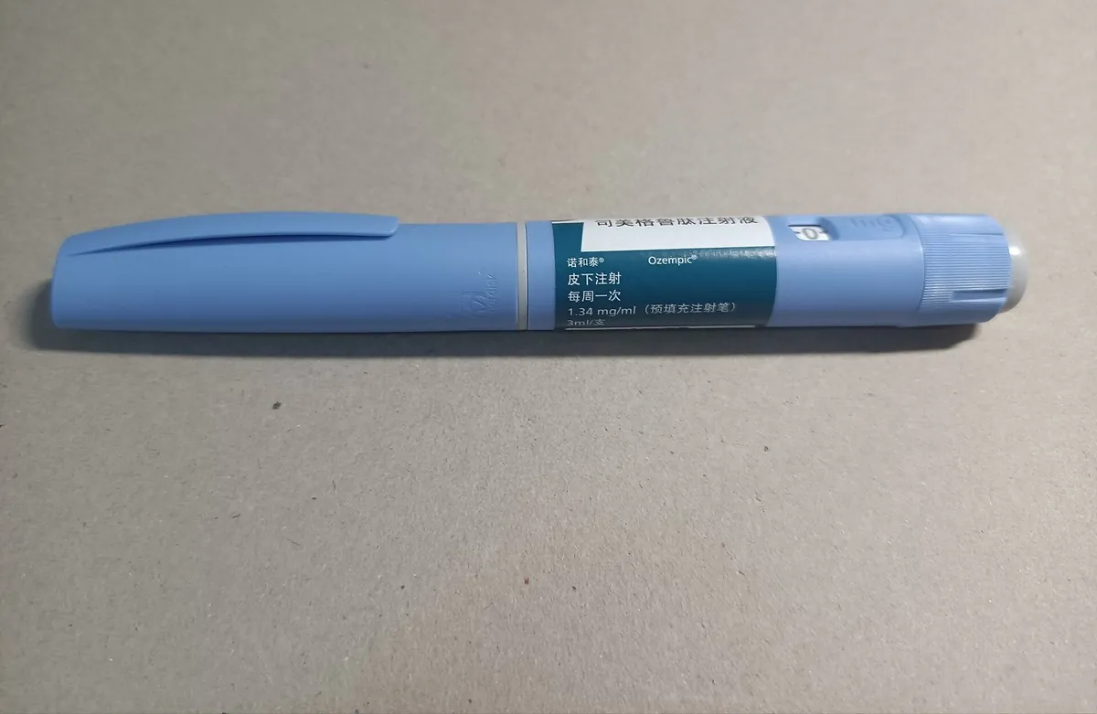 Caneta aplicadora azul de Ozempic (semaglutida) fora da embalagem, deitada sobre superfície cinza, com rótulo em chinês.