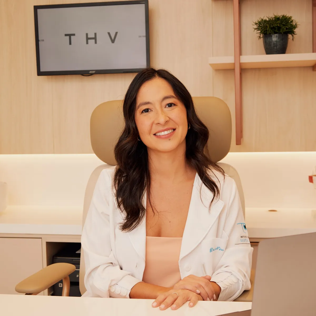 Dra. Nina Konichi sorrindo, sentada à mesa do consultório, com notebook e documentos à frente.