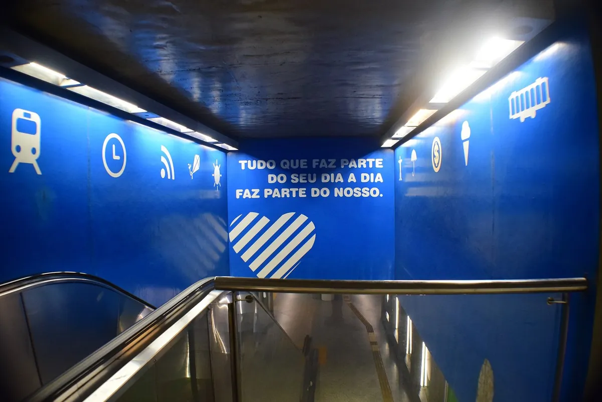 Escada rolante descendo para a plataforma da estação Uruguai do metrô, com paredes azuis e uma frase de campanha.