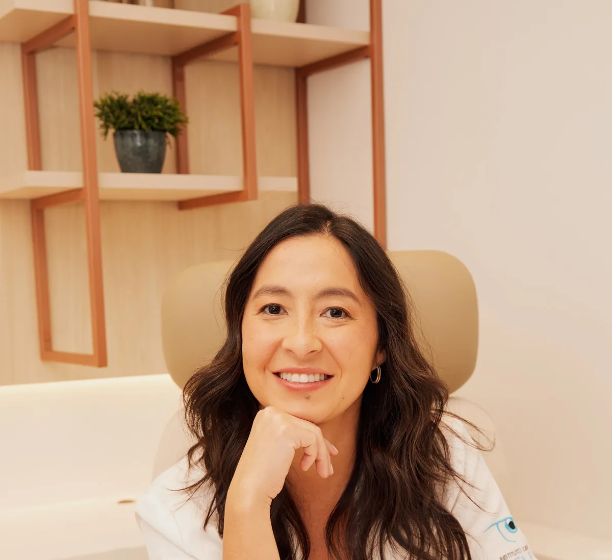 Dra. Nina Konichi sorrindo, com a mão no queixo, sentada à mesa do consultório.